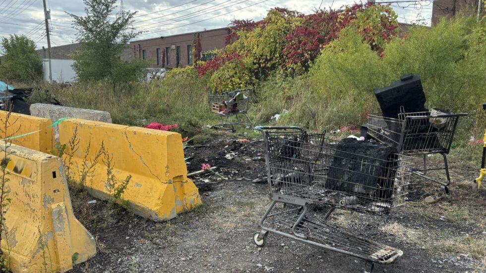 Des débris calcinés jonchent le sol sur un terrain vague, dans un campement itinérant où une femme est décédée dans un incendie.